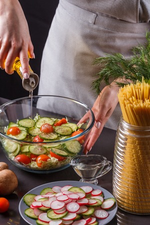 A young woman in a gray apron adds an oil to a Chinese cabbage salad.の写真素材