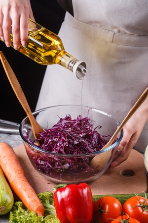 A young woman in a gray apron adds an oil to a cabbage salad.の写真素材
