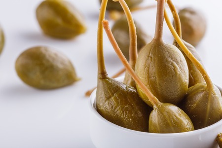 Pickled capers on a white acrylic background.