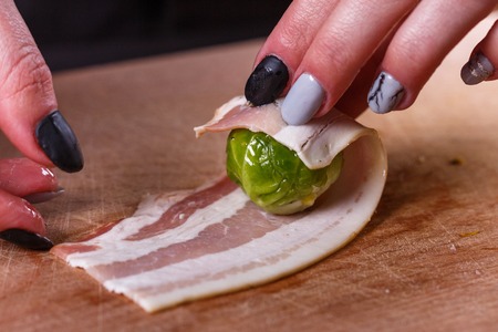 young woman wraps Brussels sprouts into bacon.の写真素材