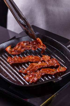 young woman in a gray apron fries bacon.の写真素材