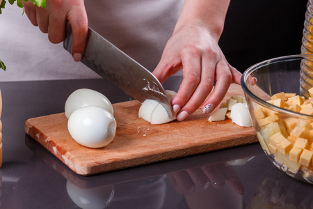young woman in a gray apron cuts a boiled egg.の写真素材