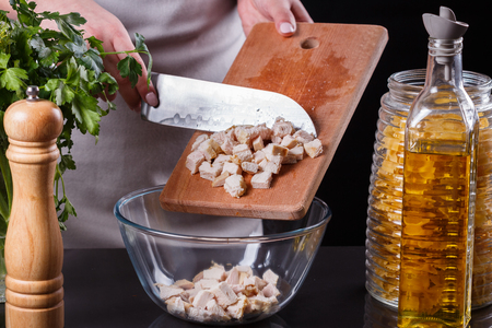 young woman in a gray apron cuts chicken breast.の写真素材