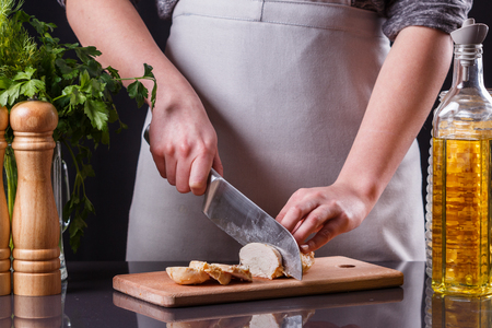 young woman in a gray apron cuts chicken breast.の写真素材