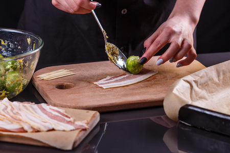 young woman wraps Brussels sprouts into bacon.の写真素材