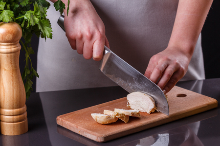 young woman in a gray apron cuts chicken breast.の写真素材