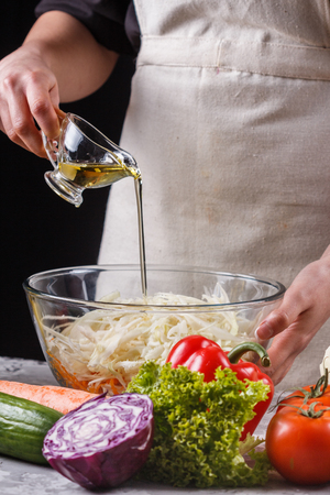 a young woman in a gray apron adds a vinegar to a cabbage salad.の写真素材