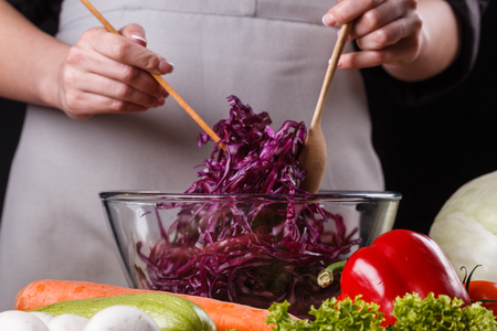 a young woman in a gray apron mixes a salad of red cabbage.の写真素材