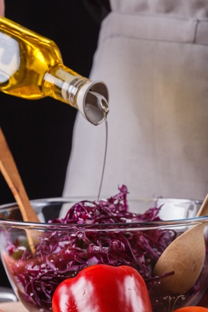 A young woman in a gray apron adds an oil to a cabbage salad.の写真素材