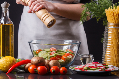 A young woman in a gray apron sipes a salad of Chinese cabbage.の写真素材