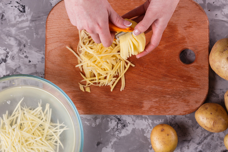 young woman in an apron cuts potatoes.の写真素材