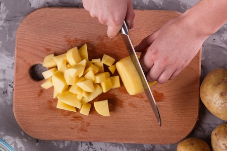 young woman in an apron cuts potatoes.の写真素材