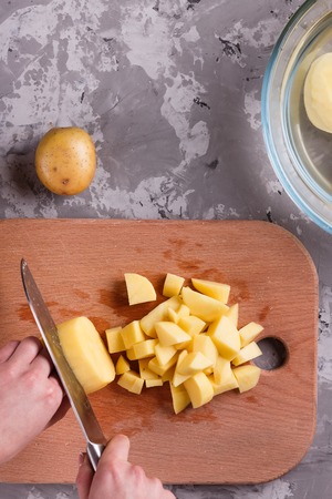 young woman in an apron cuts potatoes.の写真素材