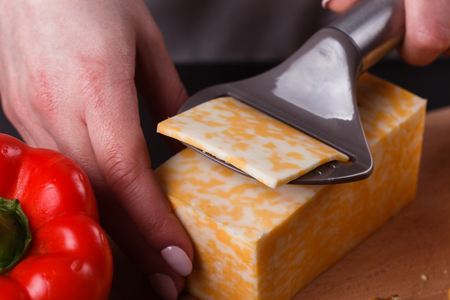 young woman slicing cheese in a gray apron.の写真素材