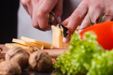 young woman slicing cheese in a gray apron.の写真素材