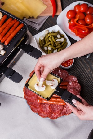 young woman is preparing a traditional Swiss cheese raclette.の写真素材