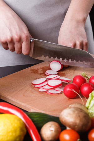 young woman in a gray apron cuts a radish.の写真素材