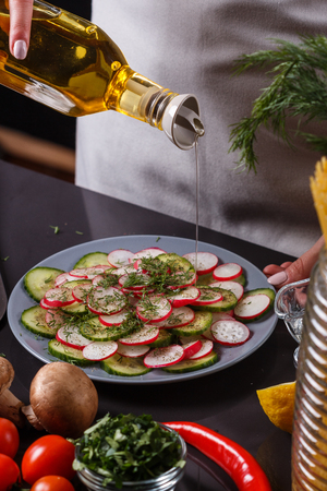 young woman in a gray apron is preparing a cucumber and radish salad.の写真素材