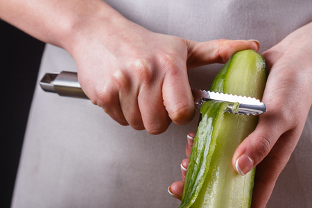 young woman in gray apron peeling cucumber.の写真素材