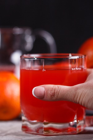 young woman in a gray apron takes a glass of juice blood orange.の写真素材