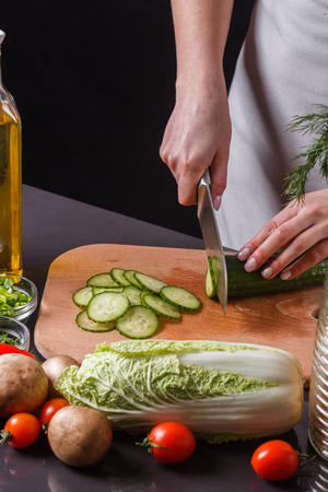 young woman in a gray apron cuts a cucumber.の写真素材