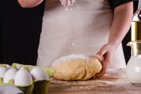 young woman in apron kneading dough on board.