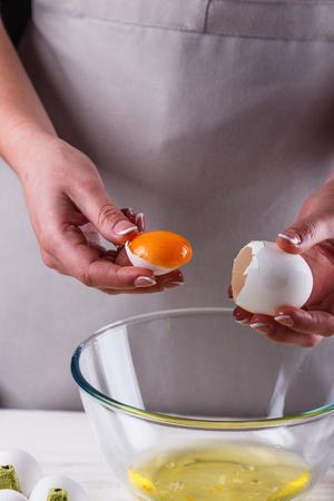 young woman in a gray aprons breaks the eggs.の写真素材