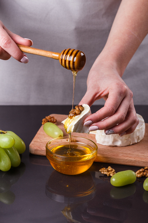 a young woman in a gray apron pouring honey Camembert cheese.の写真素材