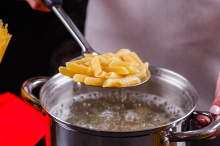 young woman in a gray apron is preparing pasta pesto.の写真素材