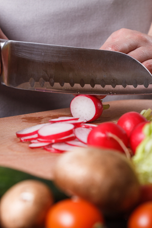 young woman in a gray apron cuts a radish.の写真素材