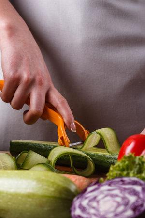 young woman in a gray apron cuts a cucumber.の写真素材