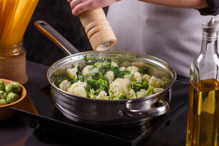 young woman in a gray apron roasts cauliflower broccoli.の写真素材