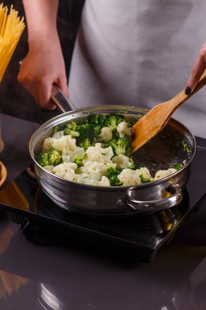 young woman in a gray apron roasts cauliflower broccoli.の写真素材