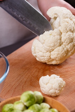 young woman in a gray aprons cuts cauliflower broccoli.の写真素材