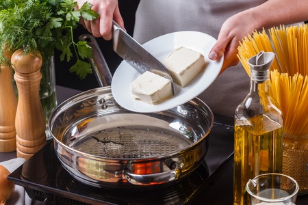 young woman in a gray apron puts butter in a frying pan.の写真素材