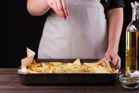 young woman seasoning potatoes on oven trayの写真素材