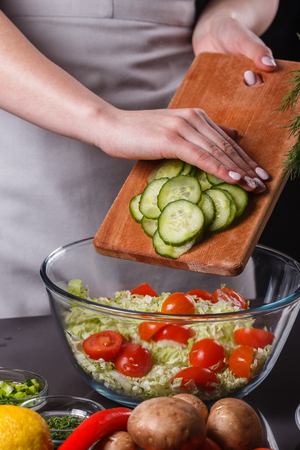 A young woman in a gray apron adds  cucumber to a salad.の写真素材