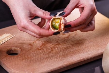 young woman wraps Brussels sprouts into bacon.の写真素材
