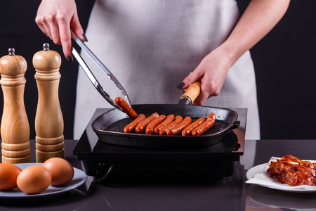 young woman in a gray apron fries sausages.の写真素材