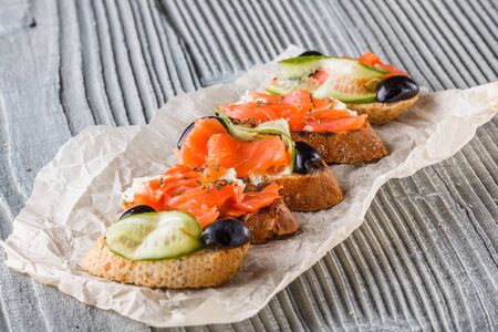 Bruschetta with smoked salmon, fresh cucumber, black olives and camembert on crumpled baking paper.の写真素材