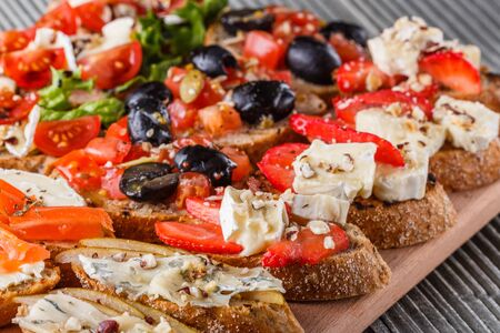 Assorted bruschetta with tomato, olives camembert blue cheese lettuce pear honey mustard balsamic vinegar cucumber on wooden boardの写真素材