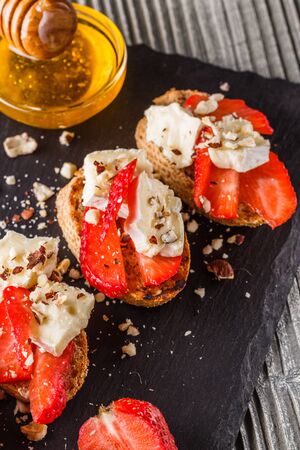 Bruschetta with strawberries, blue cheese, walnut and honey on stoyn plate.の写真素材