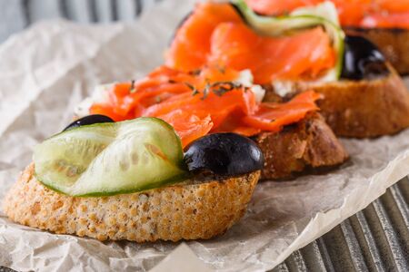 Bruschetta with smoked salmon, fresh cucumber, black olives and camembert on crumpled baking paper.の写真素材