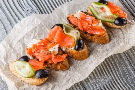 Bruschetta with smoked salmon, fresh cucumber, black olives and camembert on crumpled baking paper.の写真素材