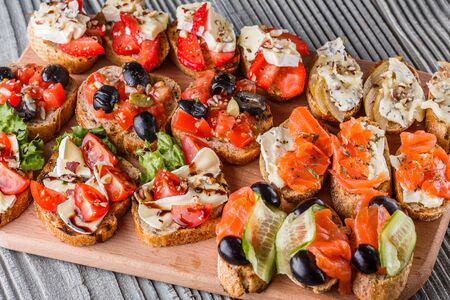 Assorted bruschetta with tomato, olives camembert blue cheese lettuce pear honey mustard balsamic vinegar cucumber on wooden boardの写真素材