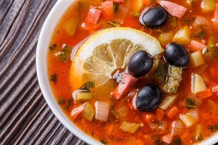 Traditional Russian meat and salt soup Solyanka in bowl on rustic wooden table.