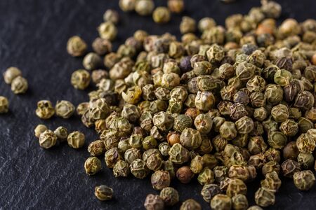 green peppercorns on dark slate stone background.
