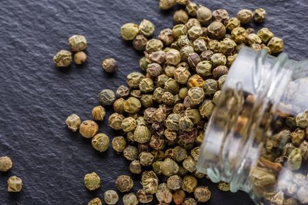 green peppercorns on dark slate stone background.