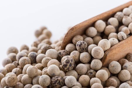 white peppercorns in wooden scoop on white background.