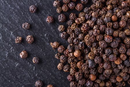 aromatic black pepper on a dark stone background.